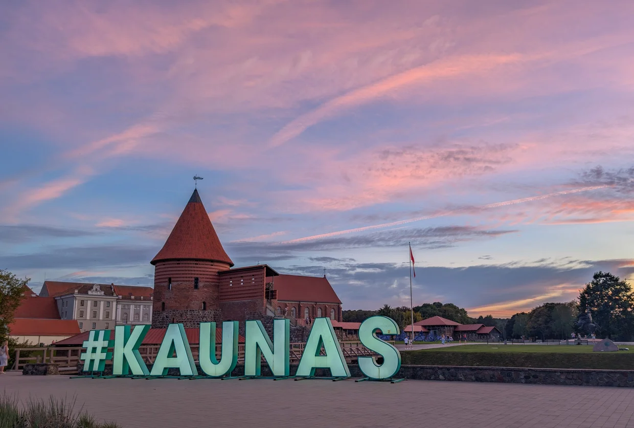 The giant #KAUNAS sign in front of the castle at sunset