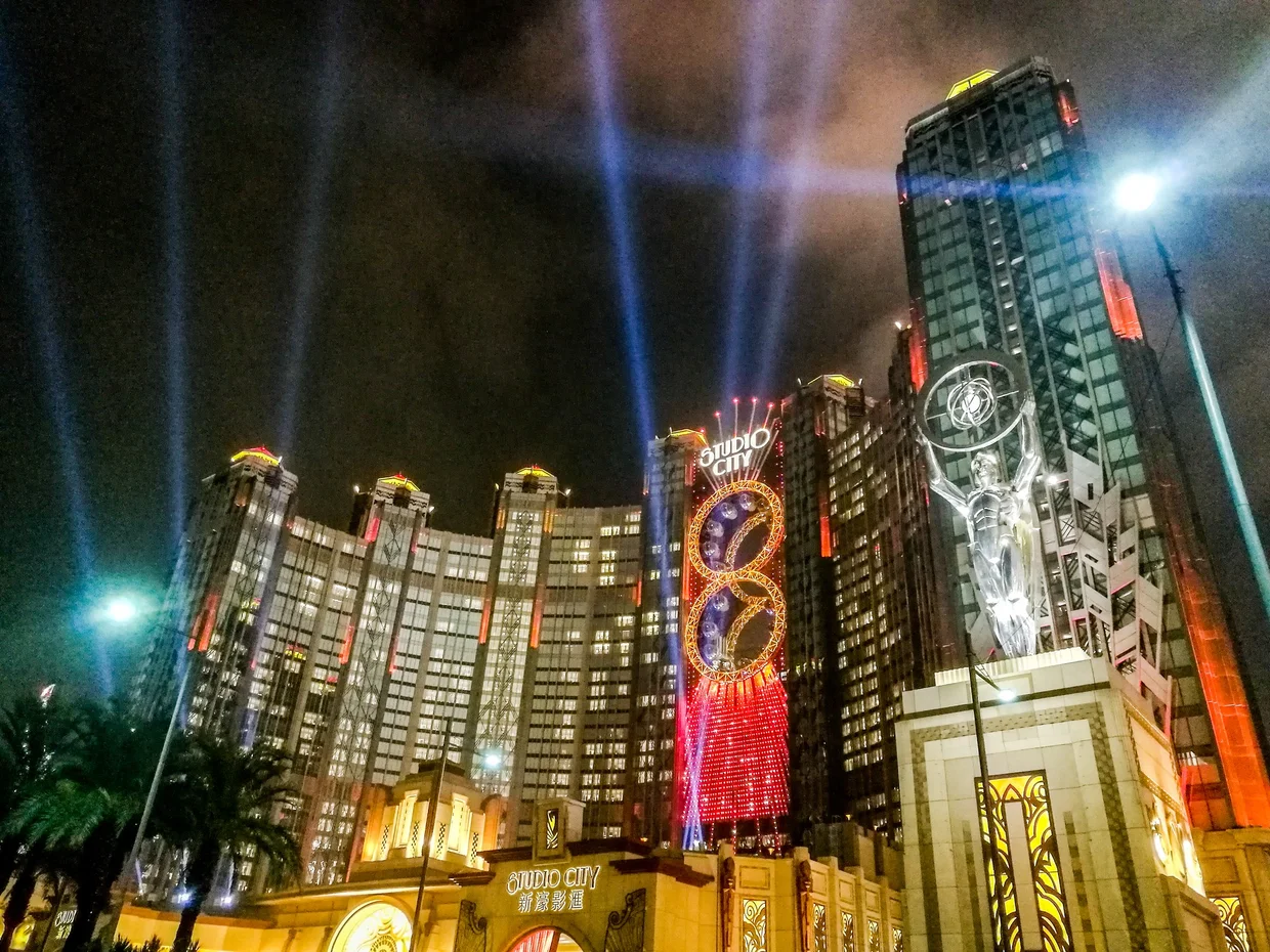 Studio City Macau casino lit up at night with spotlights and golden figure-eight ferris wheel