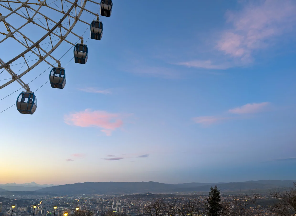 Ferris wheel at Mtatsminda Park at sunset, city spread below