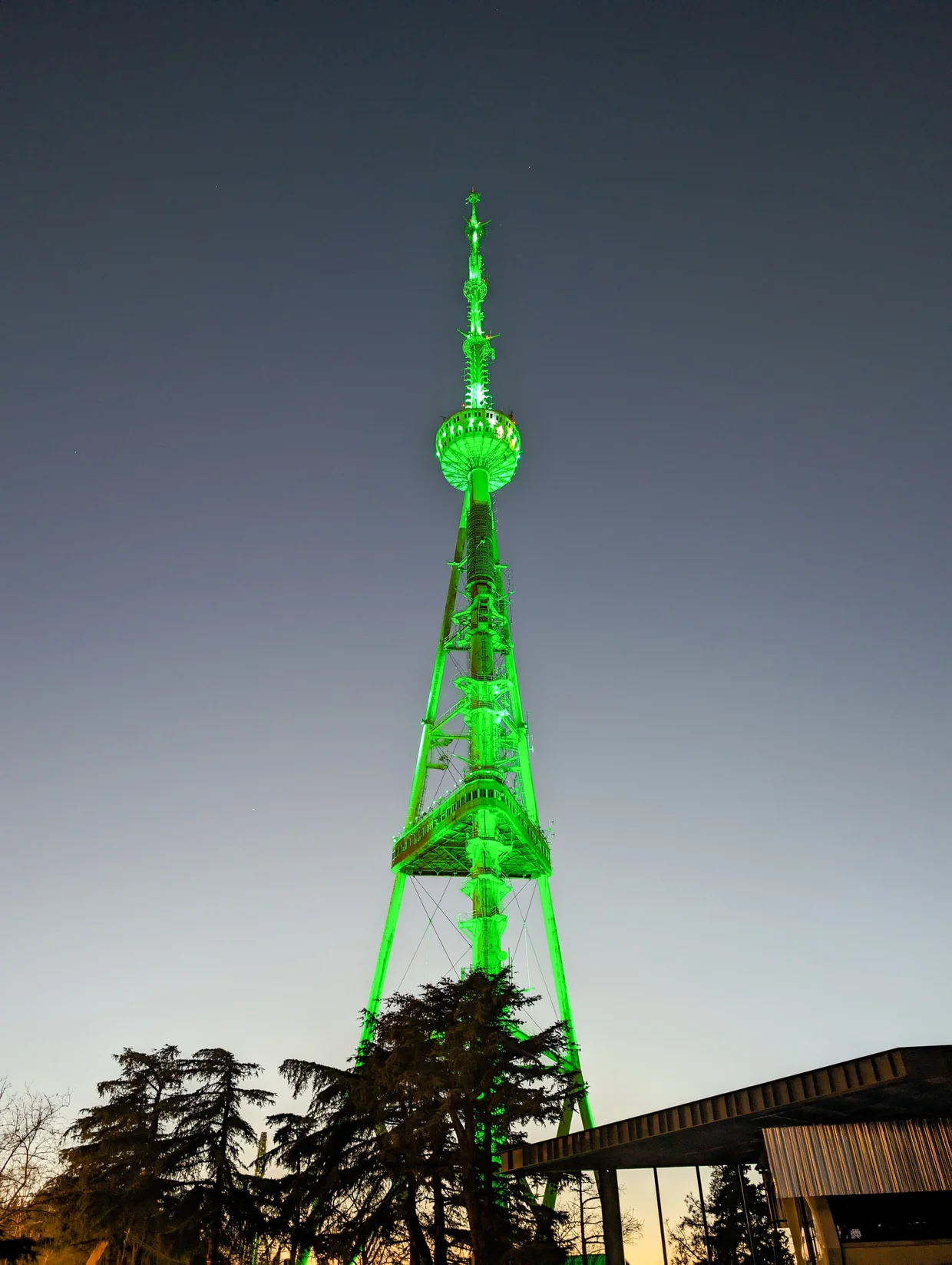 The Tbilisi TV tower lit green against the evening sky