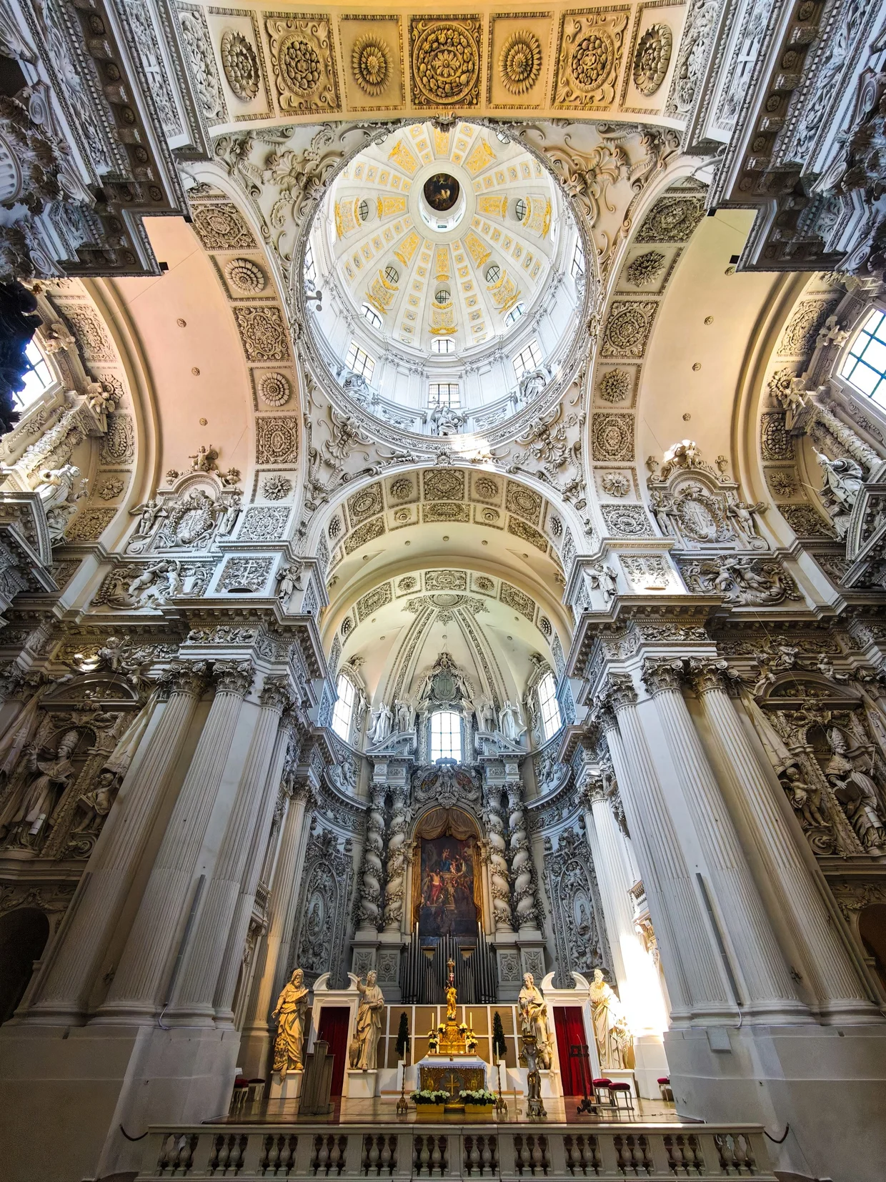 Interior of the Theatinerkirche with white stucco, columns, dome and gilded high altar