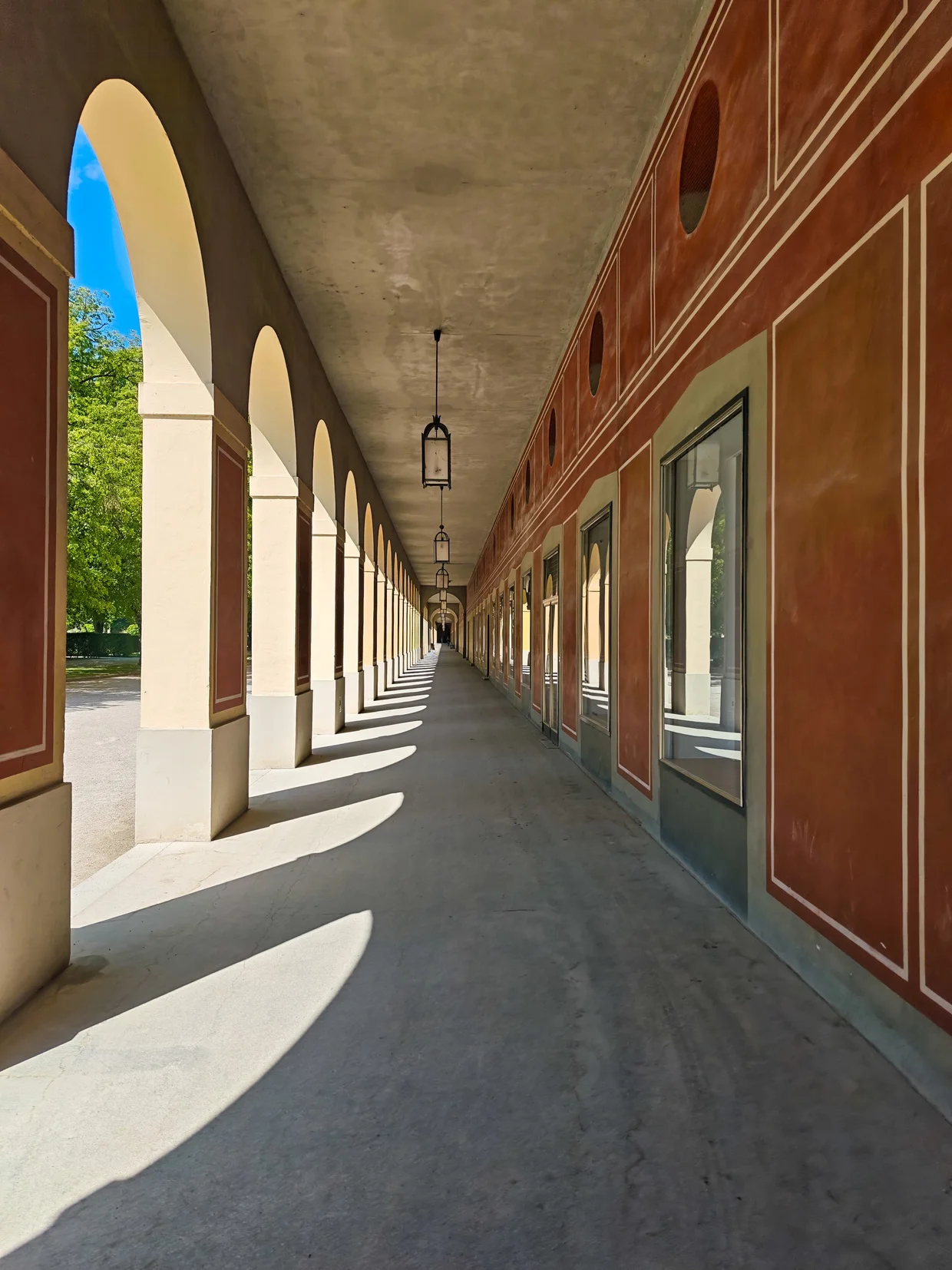 Long perspective view down the red-painted vaulted Hofgartenarkaden with hanging lanterns