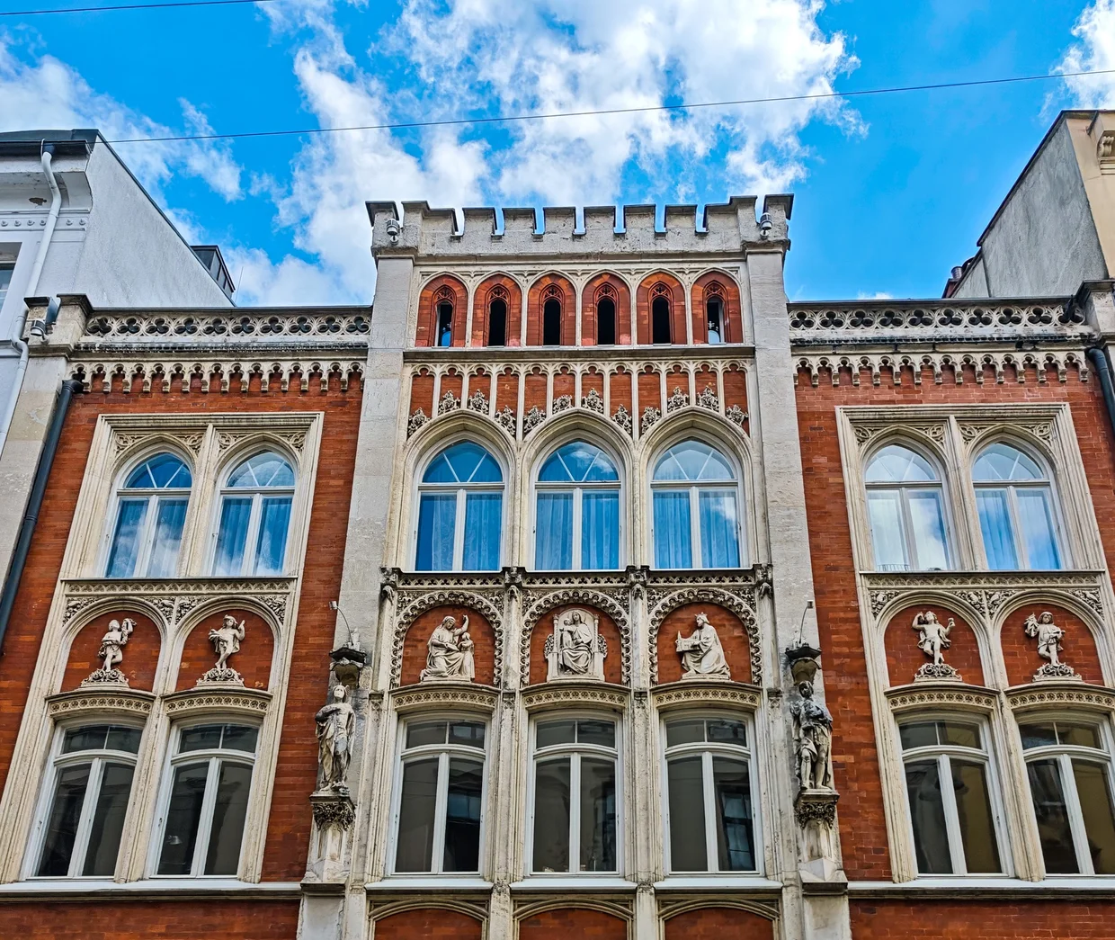 Ornate red-and-cream Gothic Revival facade with statues in niches near Pfisterstraße