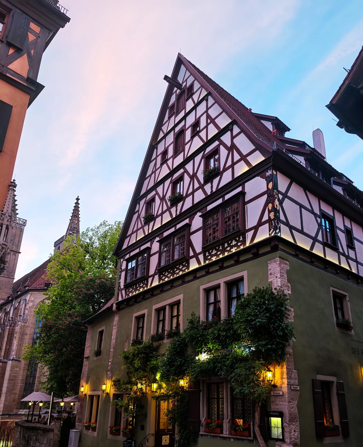 A half-timbered corner inn glowing under its lamps at dusk, St-Jakob's spire behind