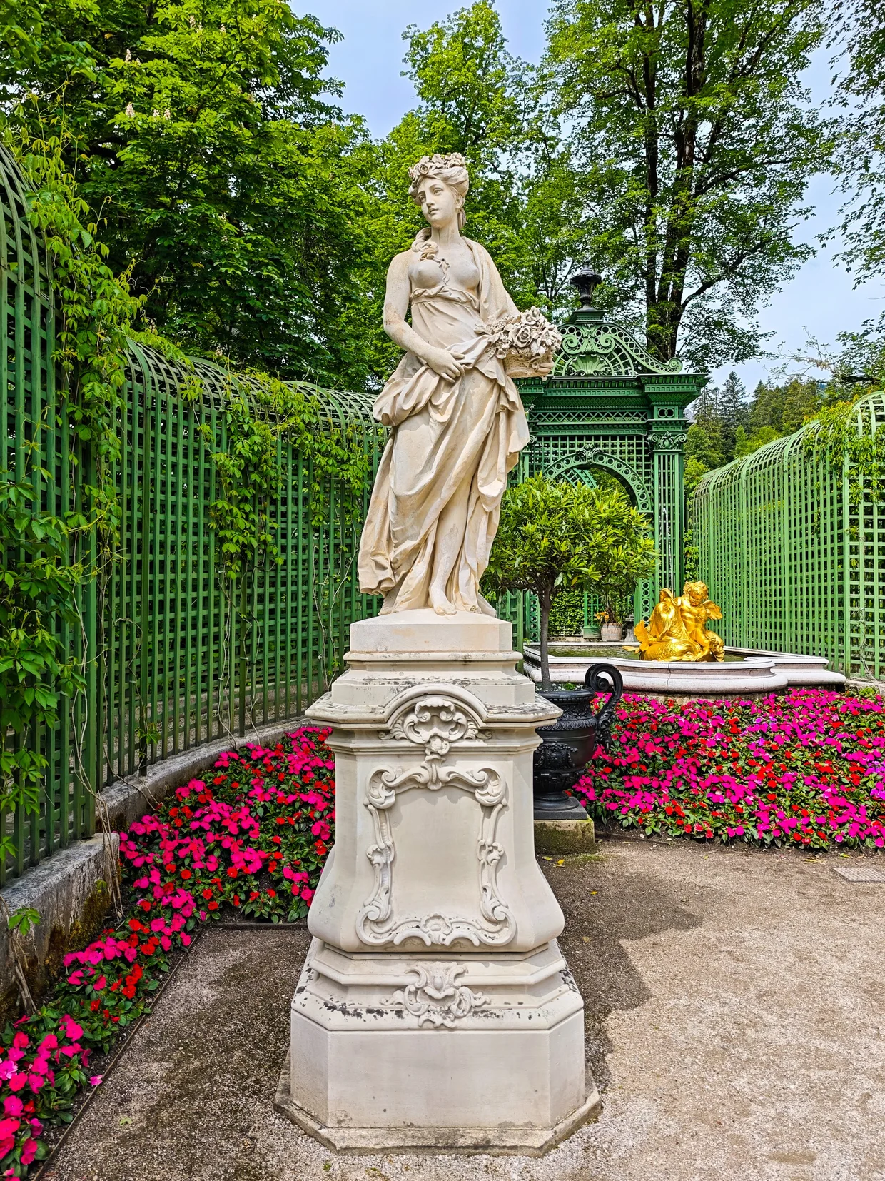 A marble garden statue with a golden putto fountain behind