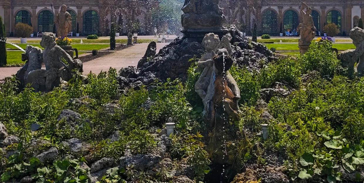 A tufa-rock grotto fountain with stone putti, the orangery arcade behind