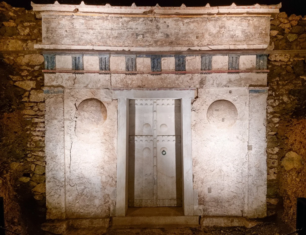 Painted facade of a Macedonian tomb with marble double doors, illuminated underground in the Vergina mound