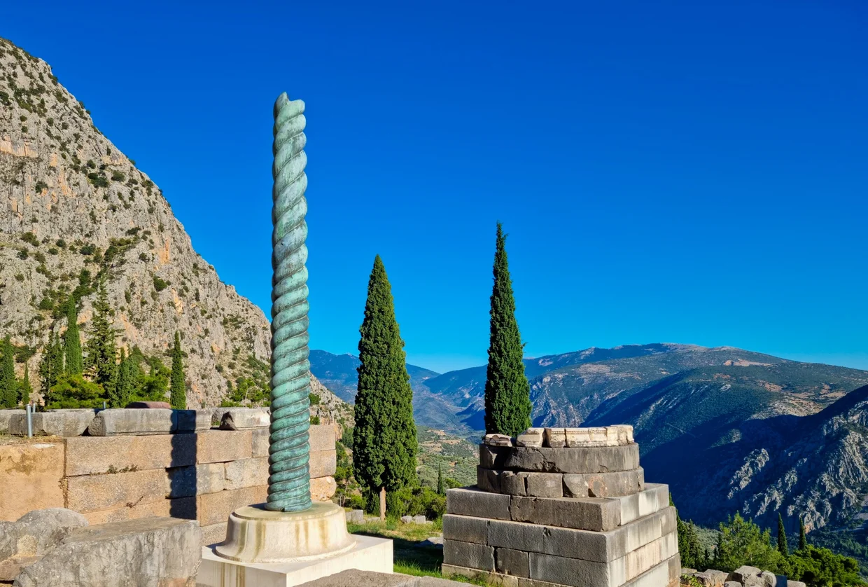 Bronze Serpent Column on its stone base with the Delphi valley falling away into the mountains beyond