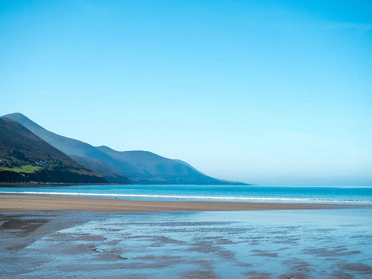 A wide Ring of Kerry beach at low tide with a mountain ridge and turquoise water