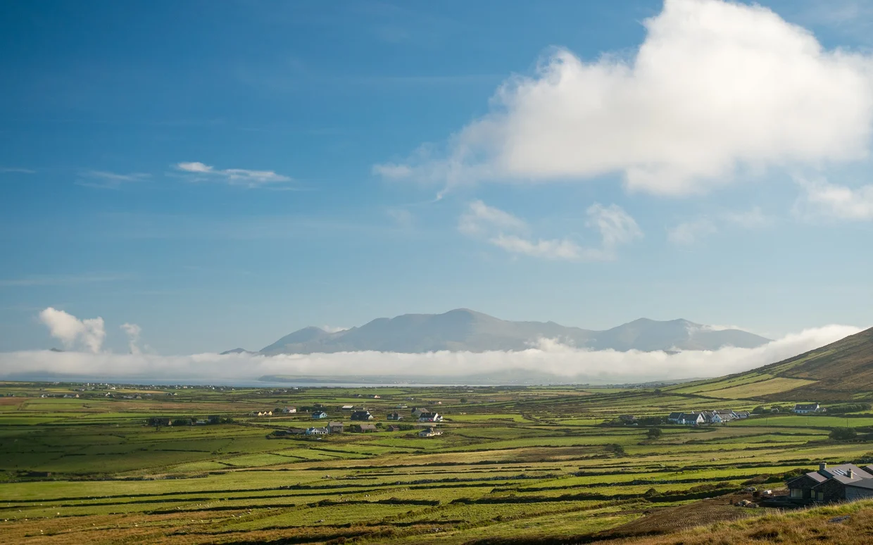 Green farmland and stone-walled fields on the Dingle Peninsula below a cloud-wrapped ridge