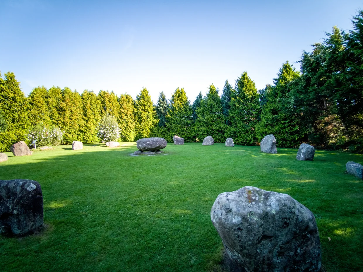 The Kenmare Stone Circle, a ring of grey boulders on a green lawn ringed by trees