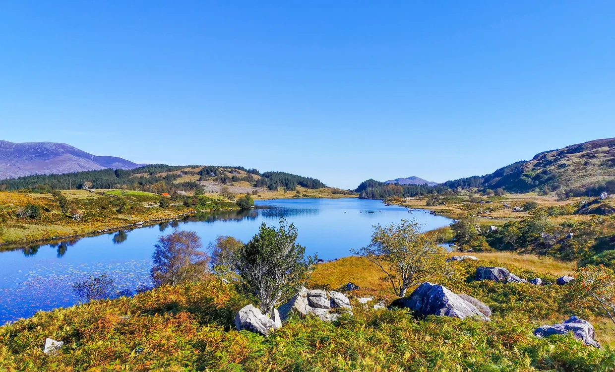 A small still lake in Killarney National Park ringed by autumn grass and low mountains