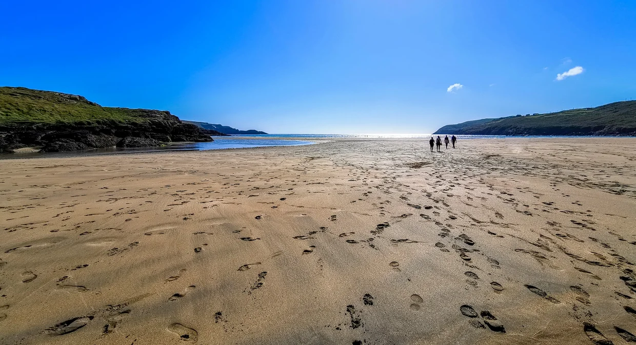 Barleycove beach at low tide with footprints in the sand and distant walkers