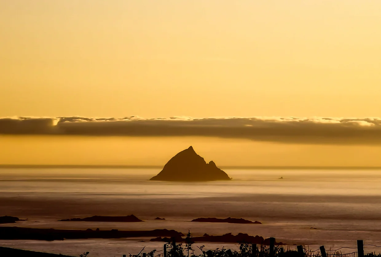 A rocky sea stack silhouetted on a golden sunset sea off the Dingle Peninsula