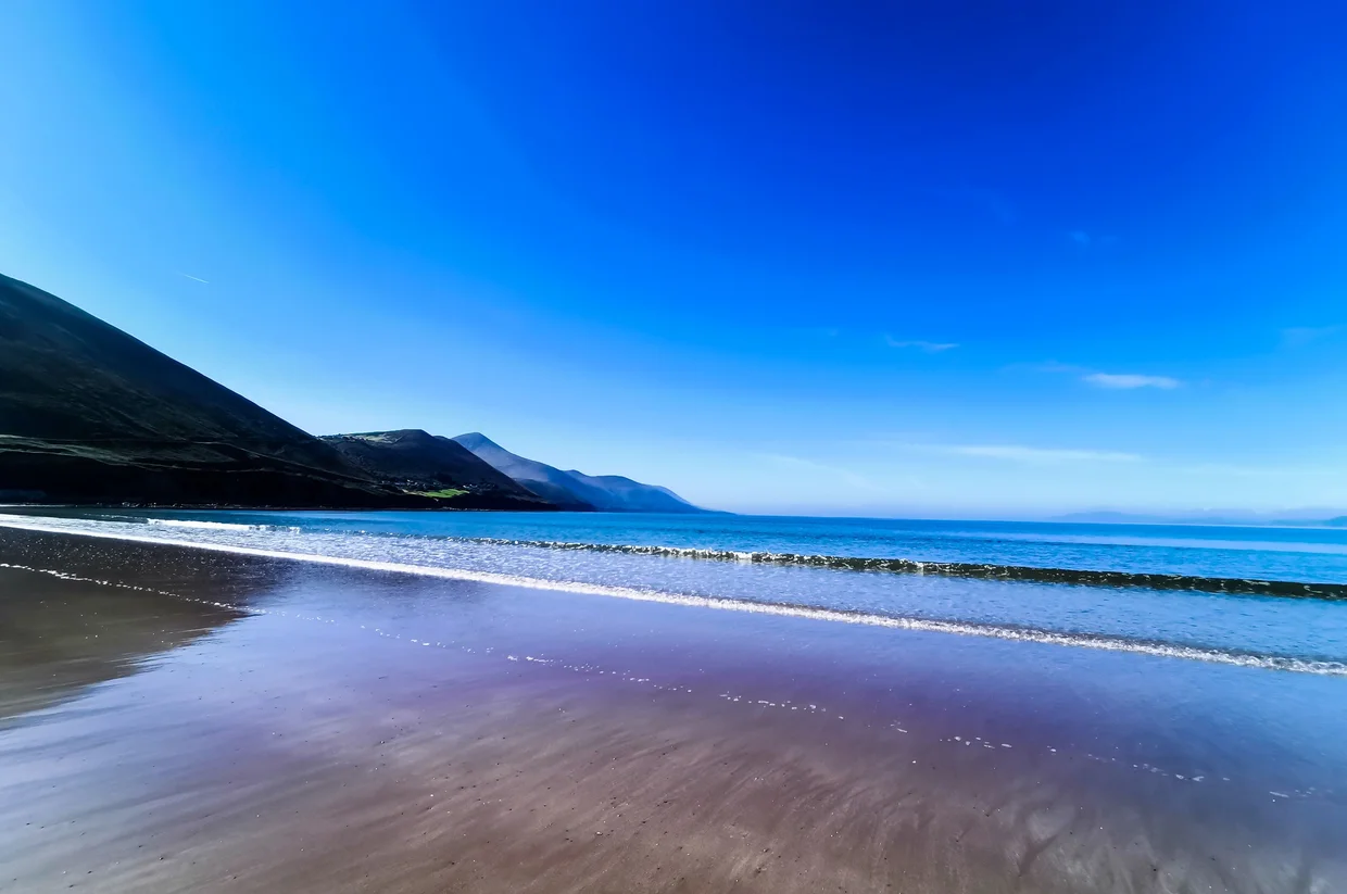 A Ring of Kerry beach with a dark mountain slope and blue sky reflected in the wet sand