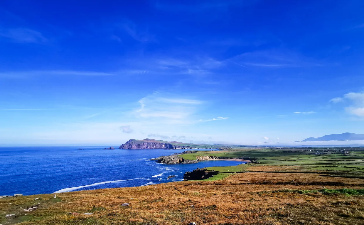 A wide sandy beach on the Dingle Peninsula below a mountain slope with turquoise water