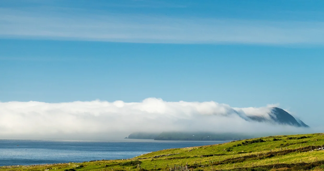Low sea cloud spilling over a headland on the Dingle Peninsula above green fields