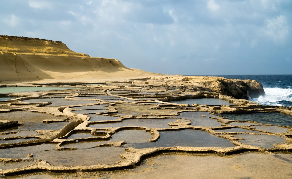 Wide view of salt pans with dramatic sandstone cliff in background