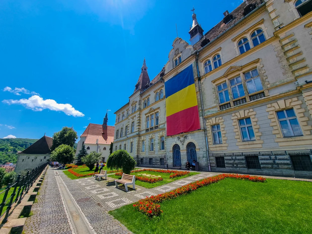 A citadel building with a big Romanian flag and a green garden