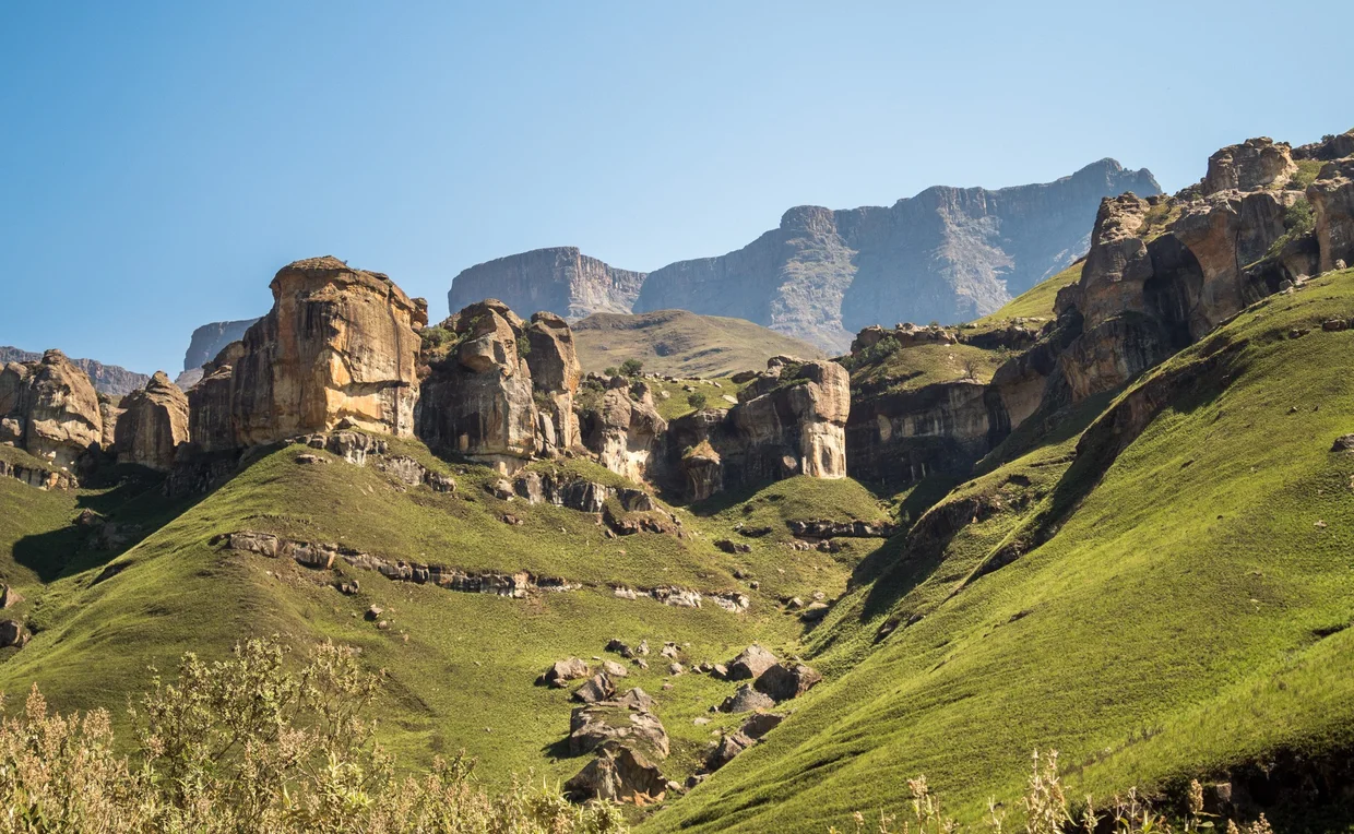 Sandstone rock formations and green slopes in the Drakensberg foothills
