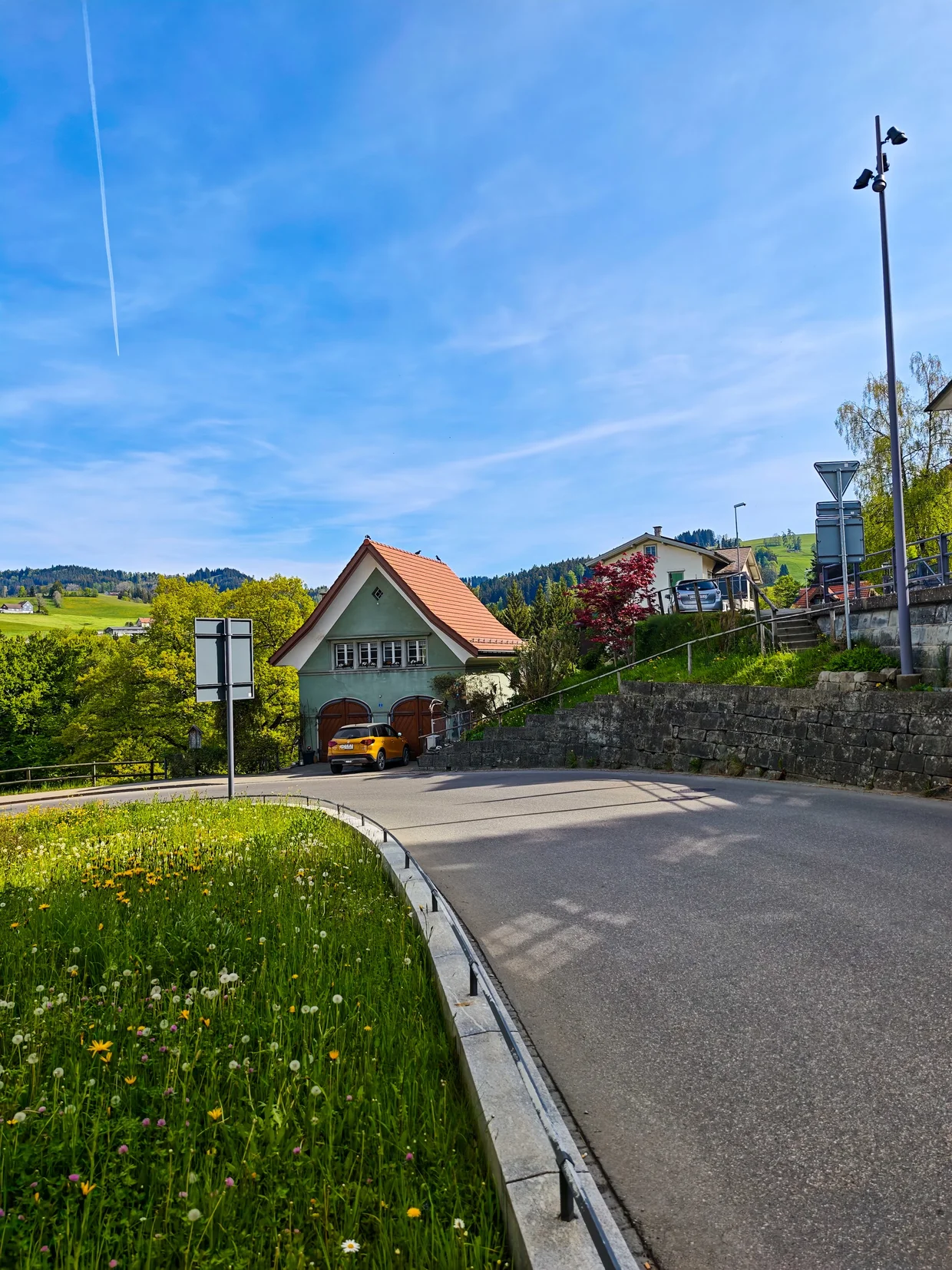 Yellow car parked next to a cream Appenzeller chalet on the road into Trogen
