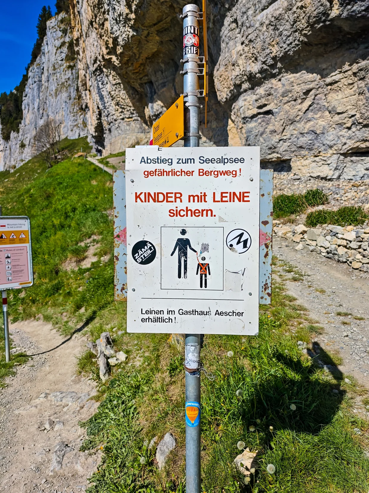 Trail sign warning Kinder mit Leine sichern at the start of the descent