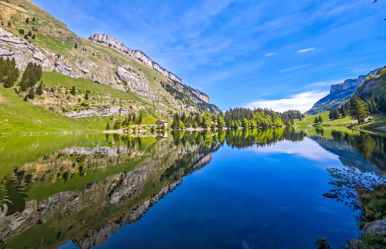 Wide panorama of Seealpsee, the surrounding cliffs doubled in still blue water