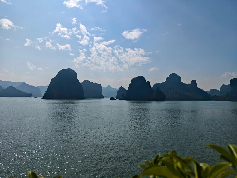 Ha Long Bay limestone pillars covered in greenery emerging from misty water, photographed from a boat