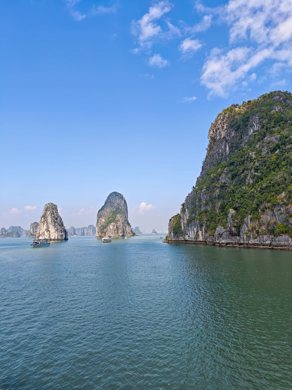 Tourist cruise boat sailing between towering limestone islands in Ha Long Bay, Vietnam